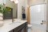 Sleek contemporary bathroom with stylish dark cabinetry, elegant lighting, and a modern shower-tub combination.