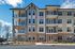 Charming apartment building exterior with stone accents and private balconies, complementing a bright blue sky backdrop.
