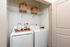 Modern laundry room featuring a sleek washer and dryer set, with stylish woven baskets on a white shelf and neatly arranged laundry essentials.