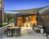 Modern outdoor lounge with sleek furniture, shaded seating area, and a stylish kitchenette under the evening sky.