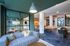 Modern lounge area featuring a plush gray sofa, large windows, and stylish pendant lighting, adjacent to a chic dining space with a unique wooden table and comfortable seating.