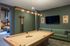 Contemporary lounge area featuring a sleek pool table, stylish green walls, and a modern seating arrangement perfect for entertainment.