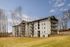 Charming residential apartment complex with spacious balconies, set against a serene backdrop of tall trees and open sky.