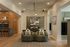 Elegant living area with modern lighting, cozy armchairs, and a chic kitchen with wooden cabinets and bar seating.