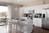 Elegant modern kitchen with sleek white cabinetry, stainless steel appliances, and a cozy island breakfast bar. Natural light enhances the open-concept space featuring stylish pendant lighting and a view of the serene outdoor patio.