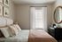 Inviting bedroom with soft neutral tones, elegant wall art, and a sunny window adorned with sheer curtains.