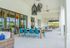 Luxurious outdoor patio featuring stylish wicker furniture, a spacious wooden dining table with vibrant teal chairs, and elegant pendant lighting, perfect for entertaining in a serene setting.