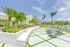 Luxurious apartment complex with tropical landscaping, modern outdoor seating, and a serene lake view under a bright blue sky.