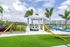 Inviting outdoor area featuring a cozy cabana with comfortable seating, vibrant green lawn, relaxing hammocks, and tropical palm trees under a bright blue sky.