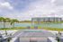 Inviting outdoor space with a modern fire pit overlooking a serene lake, surrounded by lush greenery and stylish seating, with stunning apartment building in the background.