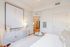 Bright and modern bedroom with stylish decor, featuring a cozy bed, elegant dresser, and a view into a sleek kitchen area.