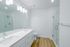 Elegant modern bathroom with sleek double sinks, a glass-enclosed shower, bright vanity lighting, and stylish wood flooring.