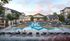 Luxury apartment complex with a stunning pool, lounging areas, and modern architecture surrounded by lush greenery.