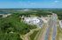 Impressive aerial view of a modern apartment complex nestled amidst lush greenery, with convenient access to major highways and serene landscapes.