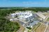 Bird's-eye view of a modern apartment complex surrounded by lush greenery and spacious parking, showcasing a vibrant community setting in a serene environment.