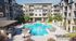 Luxurious apartment complex featuring a vibrant outdoor pool area with stylish loungers and private cabanas, surrounded by modern architecture and lush greenery.