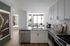 Elegant modern kitchen with sleek cabinetry, stainless steel appliances, and a bright, cozy living area visible through large windows.