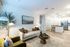 Chic open-plan living area with elegant furnishings, featuring a cozy sofa, stylish coffee table, modern kitchen, and warm ambient lighting.