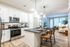 Modern open-concept kitchen and living area with sleek white cabinets, chic pendant lighting, and inviting bar seating leading to a cozy, sunlit living room.