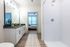 Elegant bathroom with modern double vanity, sleek finishes, and a spacious walk-in shower, leading to a sunlit bedroom.
