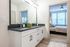 Modern apartment bathroom with elegant white cabinetry and a sleek double vanity leading to a cozy, sunlit bedroom.