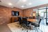 Modern conference room with sleek wooden table, leather chairs, exposed brick walls, and a wall-mounted TV, offering a stylish and professional workspace.