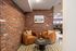 Cozy nook featuring stylish orange armchairs, a round black coffee table, and exposed brick walls, perfect for relaxation or casual conversation.