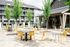 Charming outdoor patio with vibrant yellow seating and modern tables, surrounded by lush greenery and elegant apartment buildings.