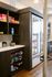 Modern pantry area with sleek wooden cabinets, stocked with vibrant snacks and essentials, complemented by a stainless steel refrigerator on warm hardwood flooring.