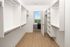 Spacious, well-lit walk-in closet with elegant shelving and a scenic view through a bedroom doorway, featuring luxurious hardwood floors.