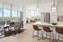Modern open-concept apartment with floor-to-ceiling windows, offering panoramic city views. Features a sleek kitchen with island seating, a bright dining area, and a stylish living space with contemporary furnishings.
