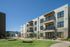 Modern three-story apartment building with balconies over a lush green lawn featuring inviting hammocks under a clear blue sky.