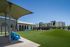 Modern apartment complex with stylish architecture, lush green lawn, and vibrant blue seating under a canopy.