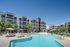 Luxurious apartment complex featuring a sparkling pool, palm trees, and stylish modern architecture under a clear blue sky.