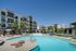 Luxurious apartment complex with a sparkling swimming pool, surrounded by palm trees and modern architecture, offering a resort-style living experience.