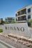 Contemporary apartment complex featuring modern architecture with spacious balconies and a welcoming sign in a vibrant community setting.