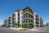 Modern apartment complex with multiple balconies, surrounded by a landscaped area under a clear blue sky.