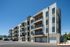 Modern multi-story apartment building with balconies and garages, set against a clear blue sky.