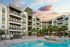 Luxurious apartment complex with modern architecture, featuring a pristine swimming pool and relaxing lounge area at sunset.