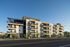 Modern four-story apartment complex with spacious balconies, surrounded by lush landscaping and clear blue skies.