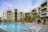 Luxury apartment complex with a sparkling pool, surrounded by palm trees and modern architecture under a vibrant, colorful sky.