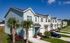 Charming row of modern townhouses with lush greenery and palm trees, set against a bright blue sky.