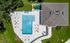 Bird's-eye view of a luxurious outdoor pool area with stylish loungers and a vibrant house roof, surrounded by lush greenery.