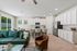 Bright open-concept living space with modern kitchen, featuring sleek white cabinets and stainless steel appliances, an inviting seating area with a plush green sofa, and large windows offering abundant natural light.