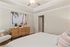 Inviting bedroom with modern decor, featuring a cozy armchair, stylish wooden dresser, and calming beach artwork.