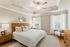 Inviting bedroom with elegant tray ceiling, cozy king-sized bed, and stylish wooden furniture, enhanced by natural light from large windows and soft, neutral tones.