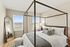 Bright and airy bedroom featuring a modern four-poster bed, elegant floor mirror, and large windows with scenic views, complemented by cozy decor.