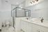 Bright and spacious bathroom featuring a modern glass shower, elegant double sink vanity, and sleek marble tiles.