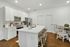 Modern kitchen featuring sleek white cabinetry, stainless steel appliances, and a spacious island with wicker stools, adjacent to a cozy dining area with elegant wooden chairs.