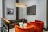 Chic modern lounge with elegant brown leather sofa, vibrant orange chairs, and striking contemporary artwork under a luxurious gold chandelier.
